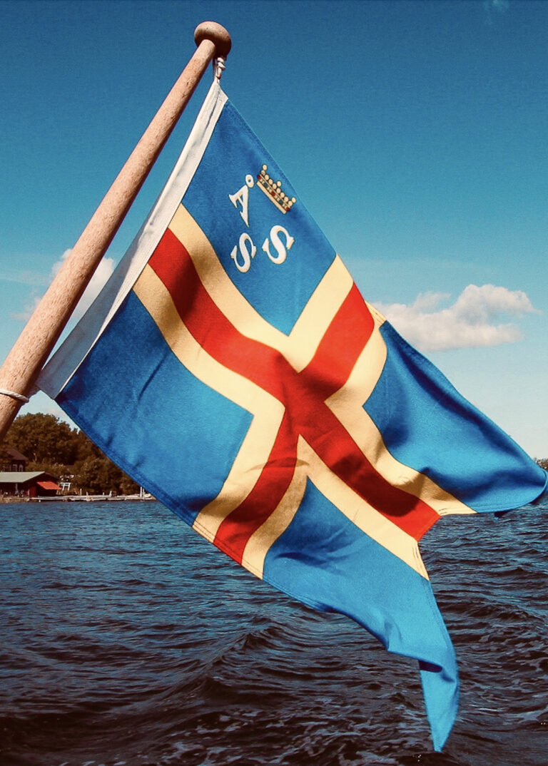 S3 E2: Rowing to a secret Baltic island The Åland Islands flag flies on a boat heading for an uninhabited islet in the Baltic Sea. © copyright Matthew Brace